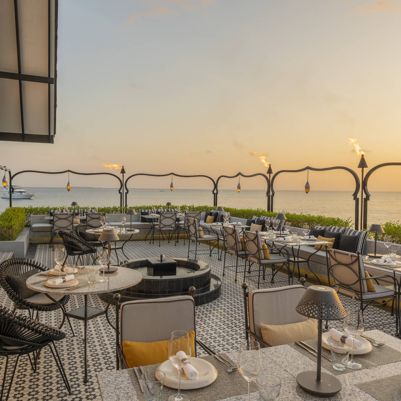 Outdoor terrace of Al Barakat at sunset with round and square tables, rattan chairs, string lighting