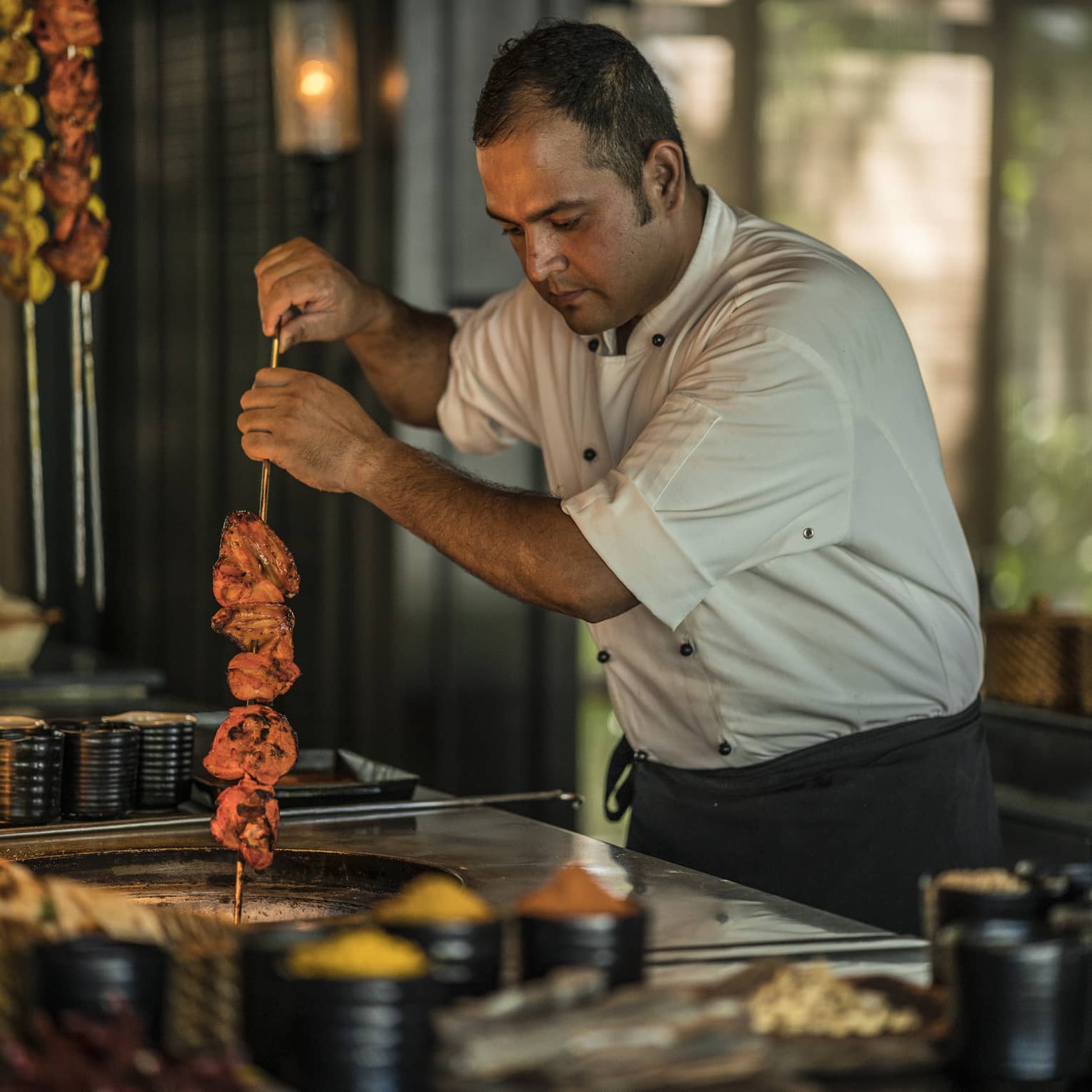 Cafe Nam Hai chef holds skewer with meat over pan
