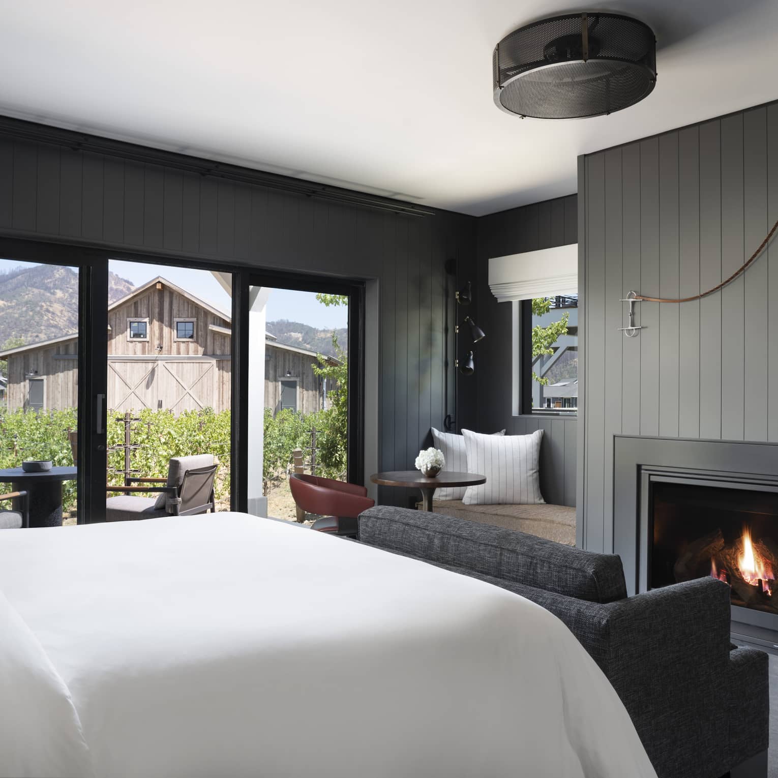 Luxury resort room with a king bed, cozy fireplace, vineyard view, seating area and outdoor patio facing rustic barn and mountains