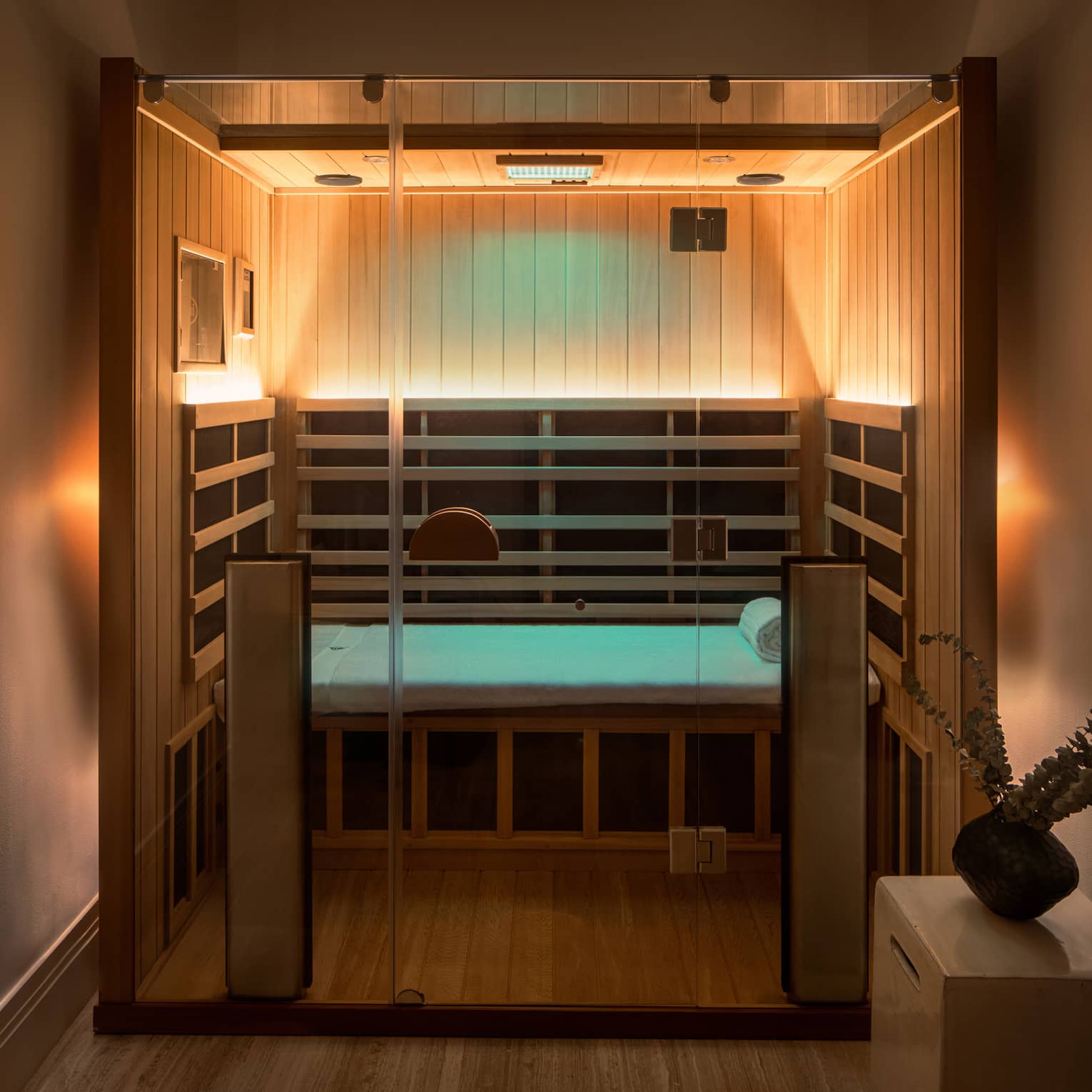 Wooden infrared sauna with lowlighting, side table with vase of eucalyptus 
