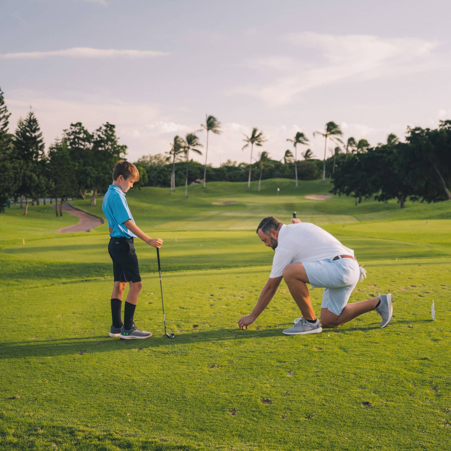 Man and young son play golf on the green, blue sky and palm trees in background 