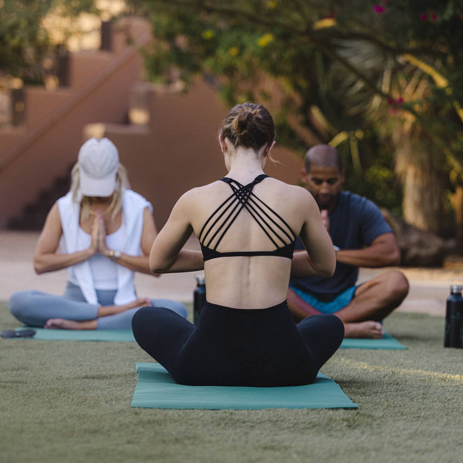 Three people doing outdoor yoga on green yoga mats.