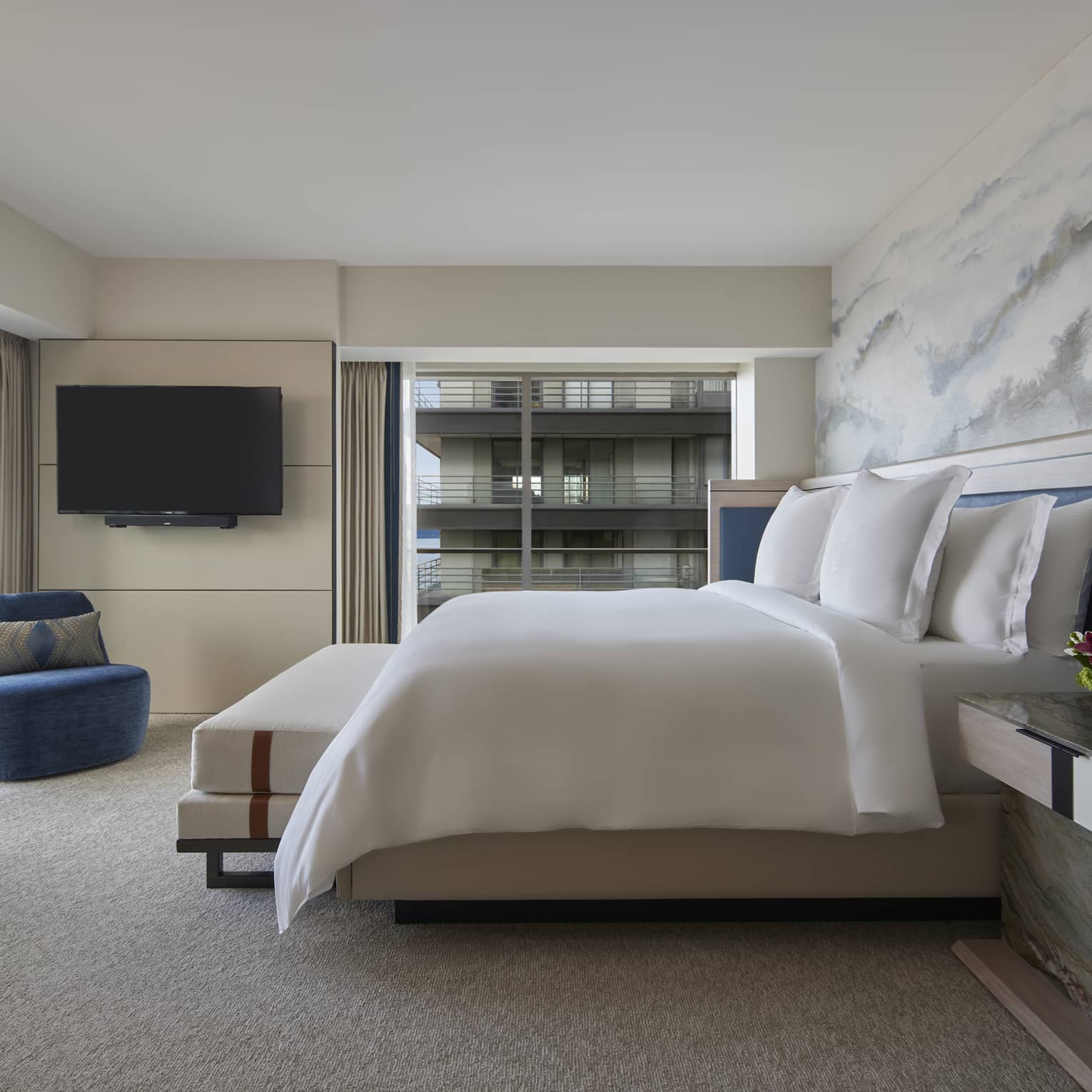Bedroom with king bed, cloud-like accent wall, two royal blue chairs and wall of windows
