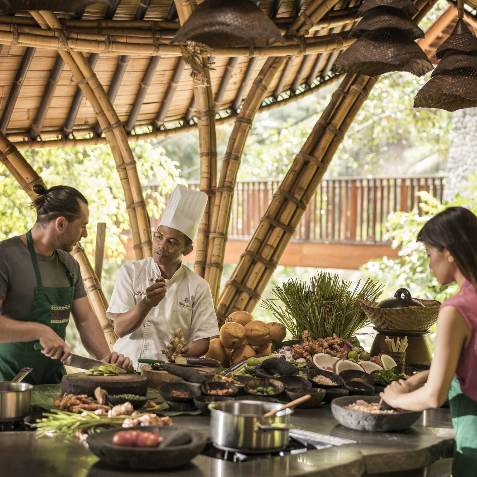 A four season chef instruction a man and woman how to cook in an outdoor kitchen