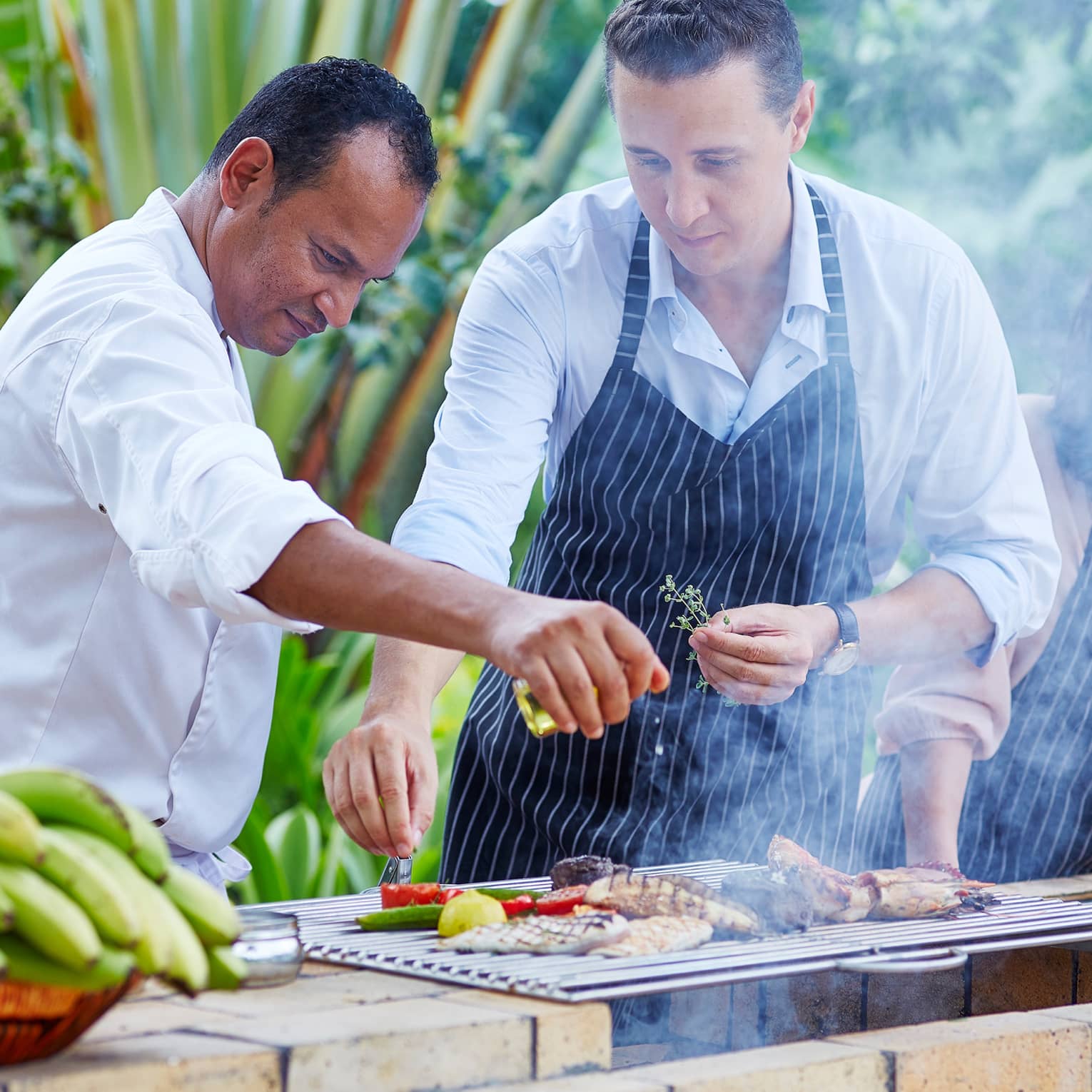 Chef, couple wearing aprons garnish meat, vegetables on outdoor grill