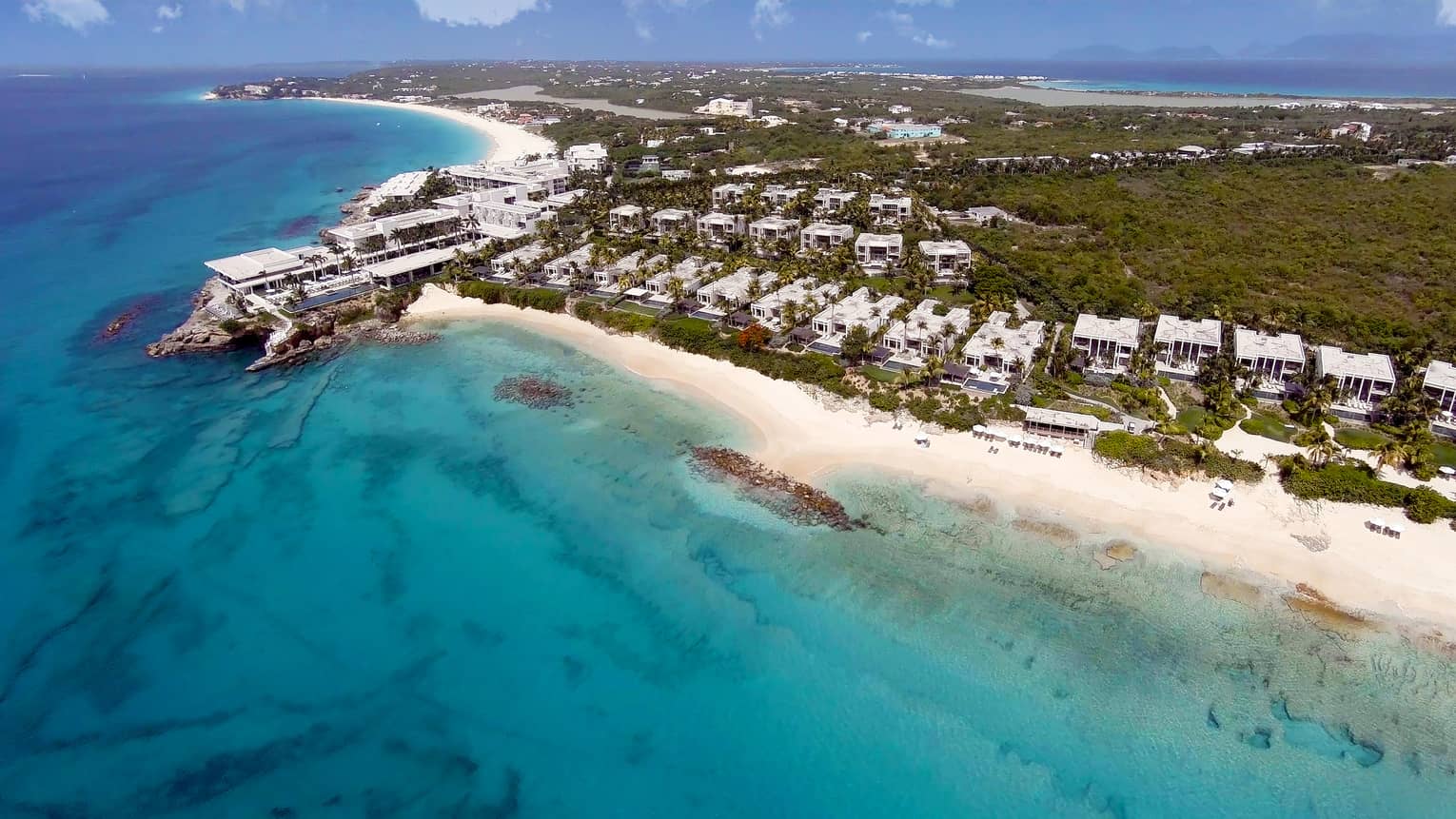 Aerial view of a luxury beachfront resort with white sand beaches, turquoise ocean water and lush greenery 
