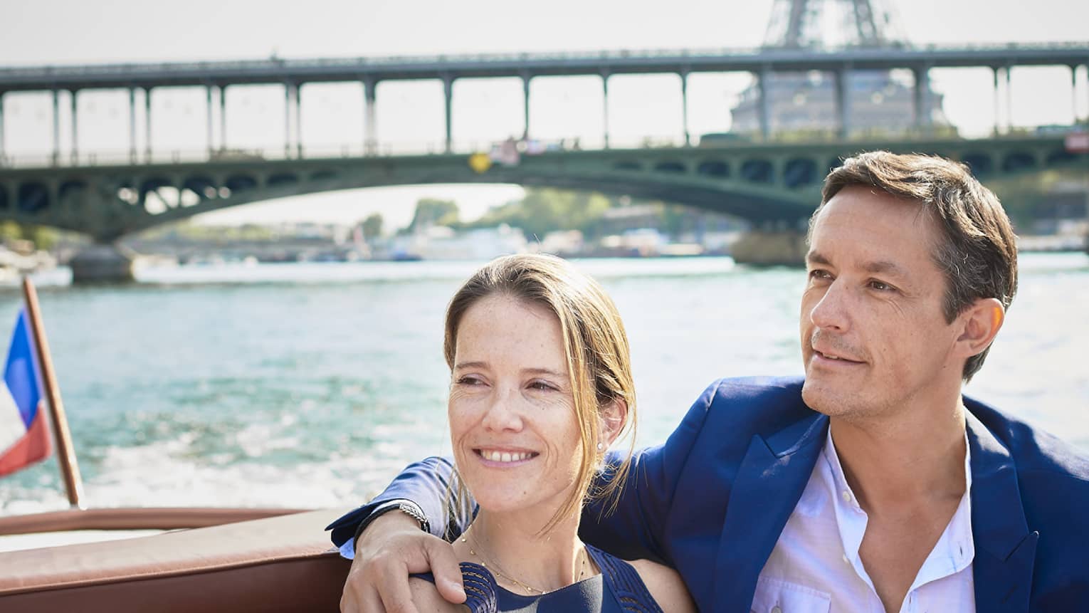 Extreme close-up of a smiling couple on a boat sharply contrasted against a blurred river, bridge and the Eiffel Tower.