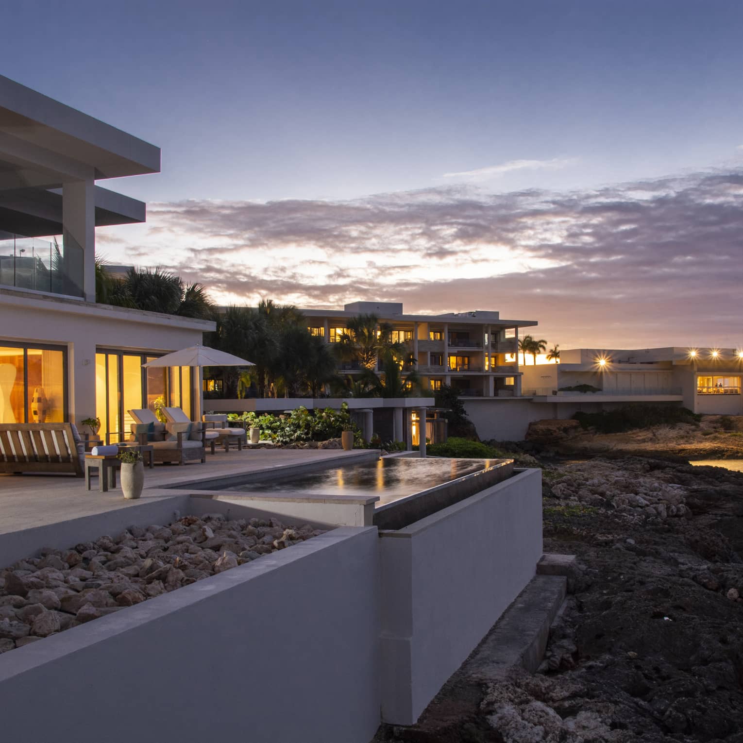 The exterior of a beachside hotel with orange lights coming from floor to ceiling windows.