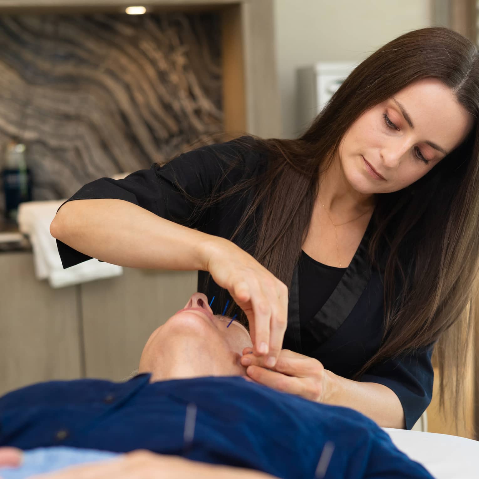 Woman performs acupuncture on person's face at luxury resort spa