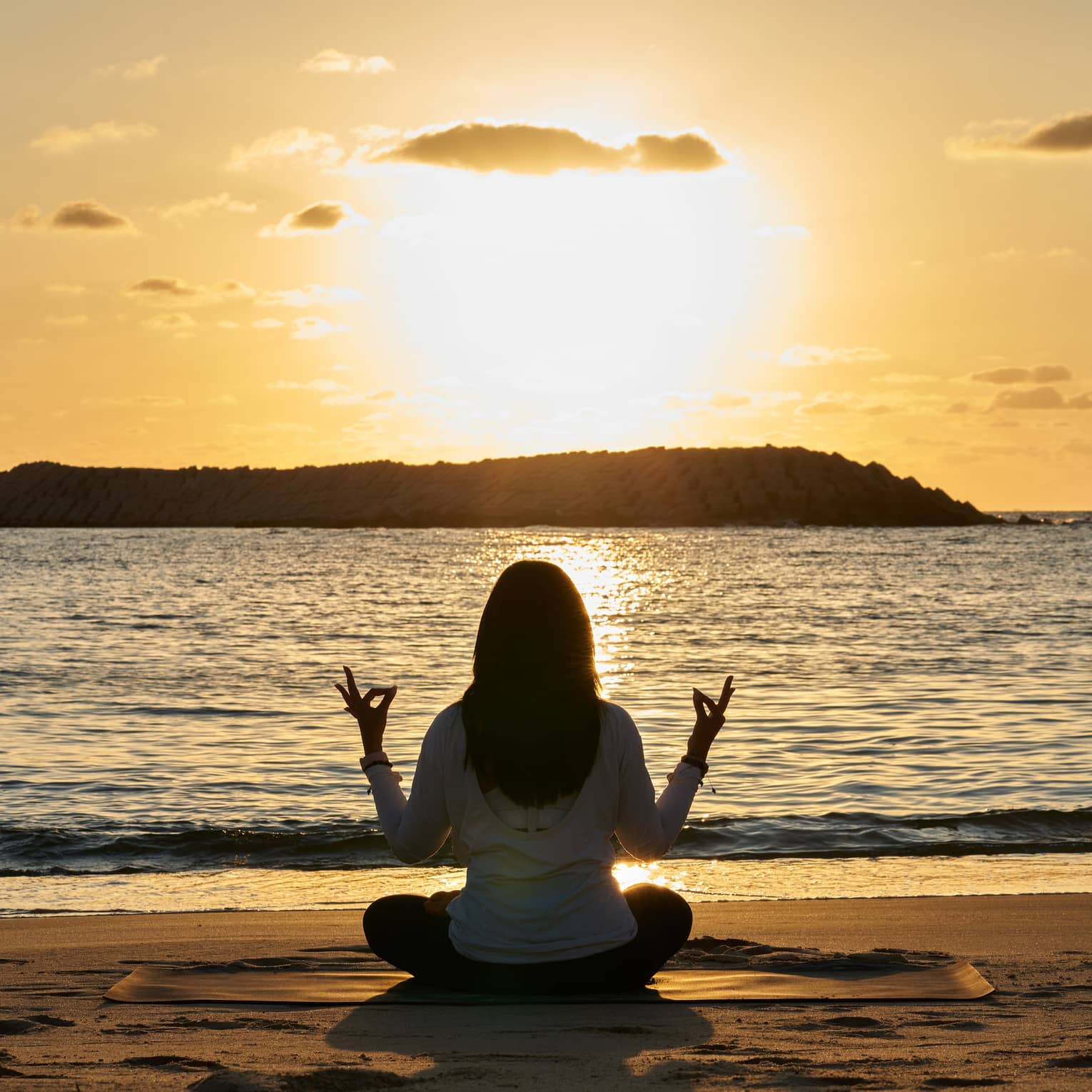 Woman meditates beachside at sunset