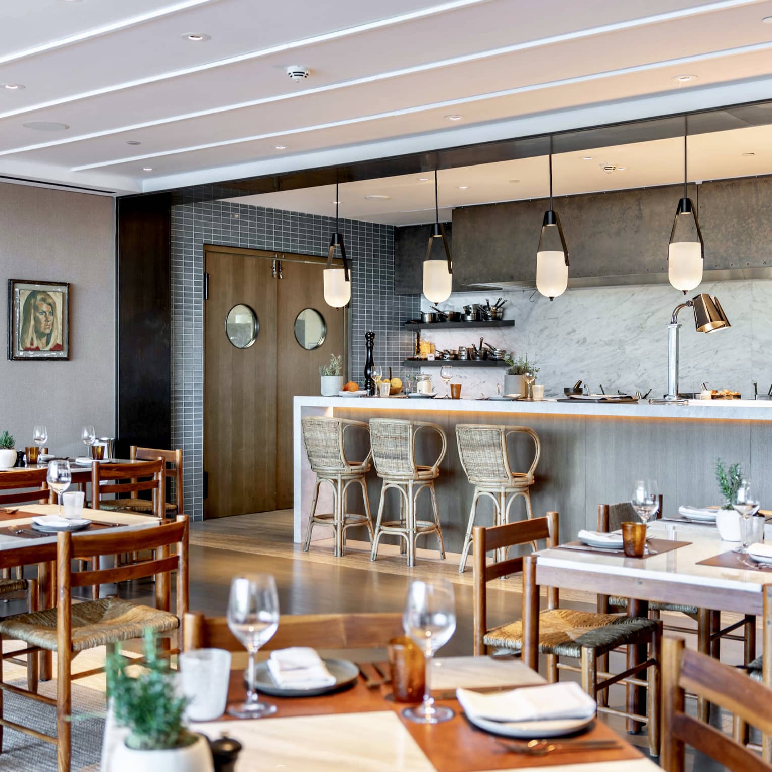 Indoor restaurant with wooden tables and chairs, bar with three wicker seats and pendant lights