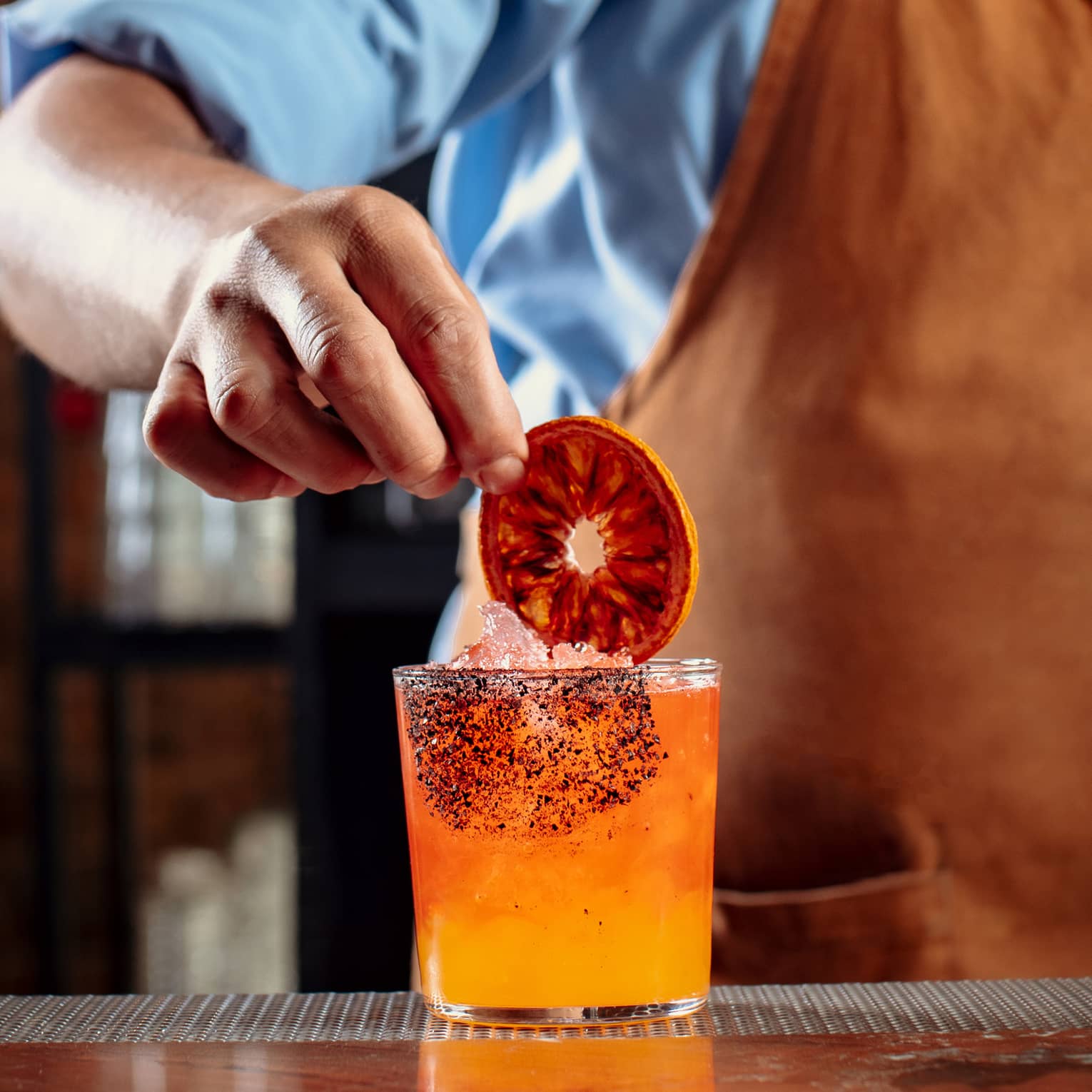 A bartender making an orange cocktail and putting a dark orange wheel in it.