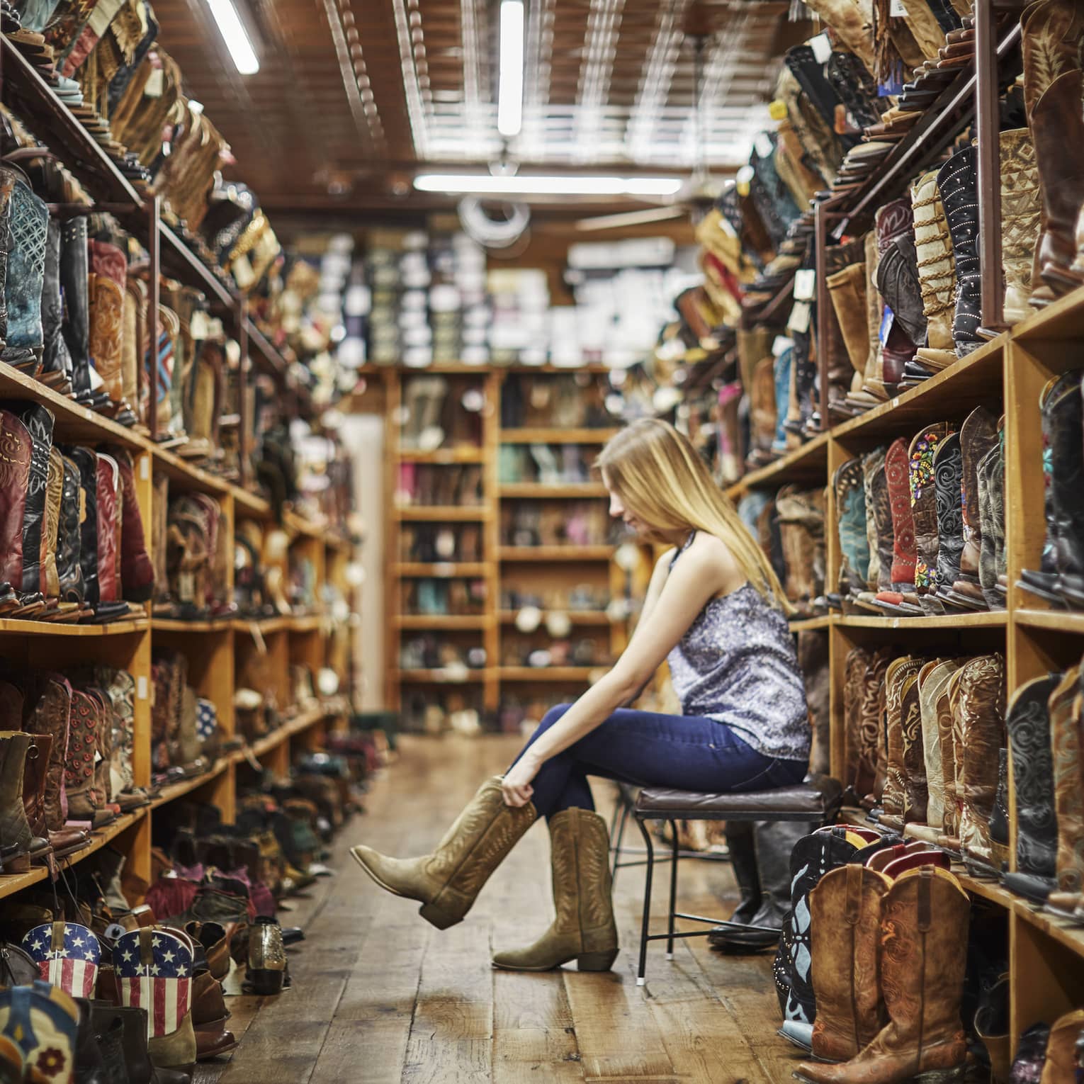 A woman trying on cowboy boots in a store full of them.