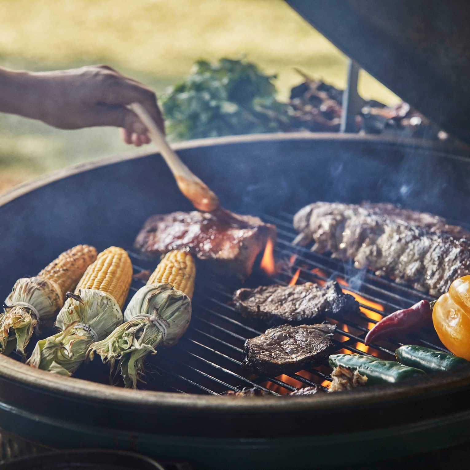 Close-up of chef brushing sauce on ribs on outdoor barbecue with corn, steaks, vegetables