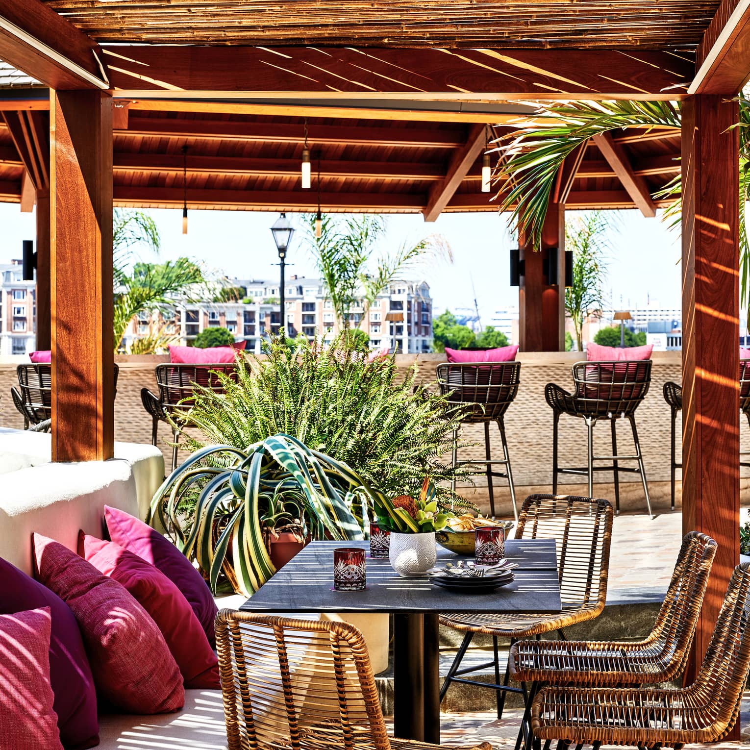 An outdoor eating venue with red cushions on benches and stools surrounded by red pillars and trees.
