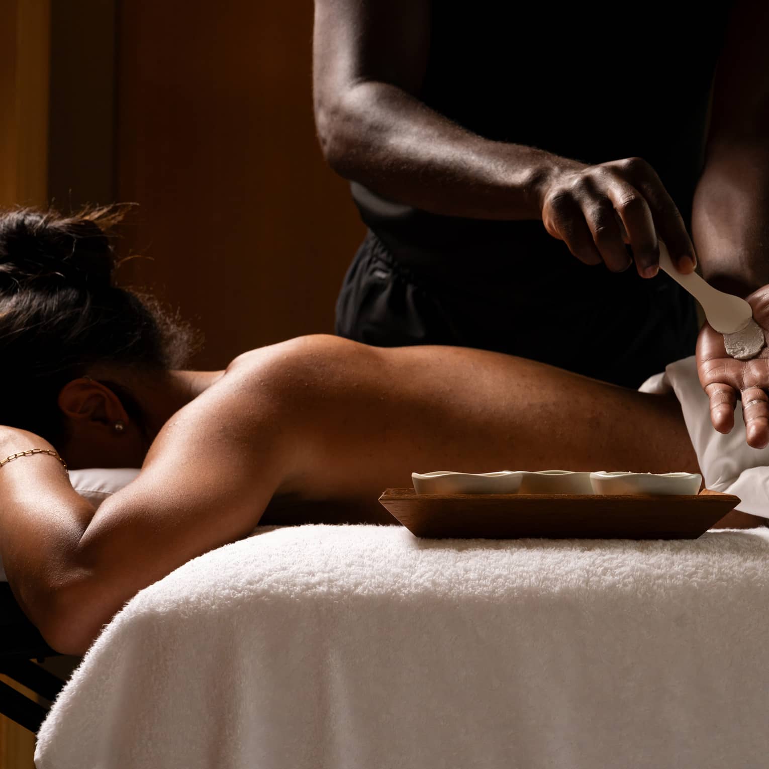 Guest laying on a massage table while the massage therapist prepares ingredients for massage.