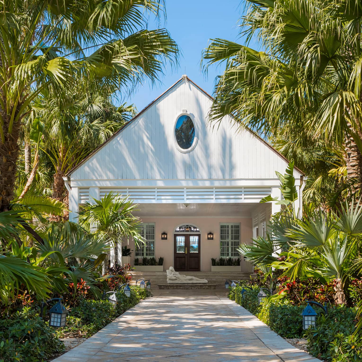 White A-frame Spa entrance with stone statue at lantern and palm-lined path on sunny day