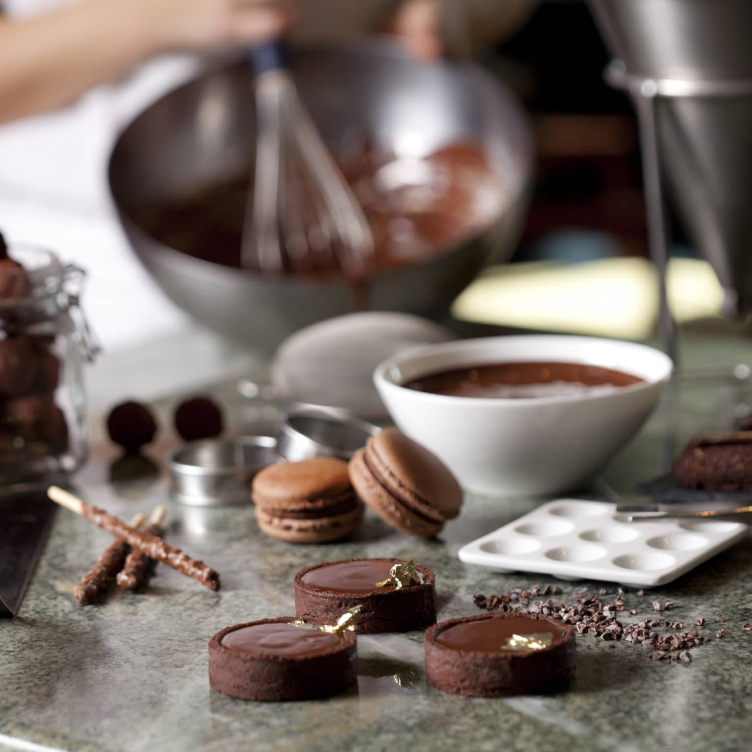 Close-up of fine chocolates, macarons, bowl of melted chocolate on counter