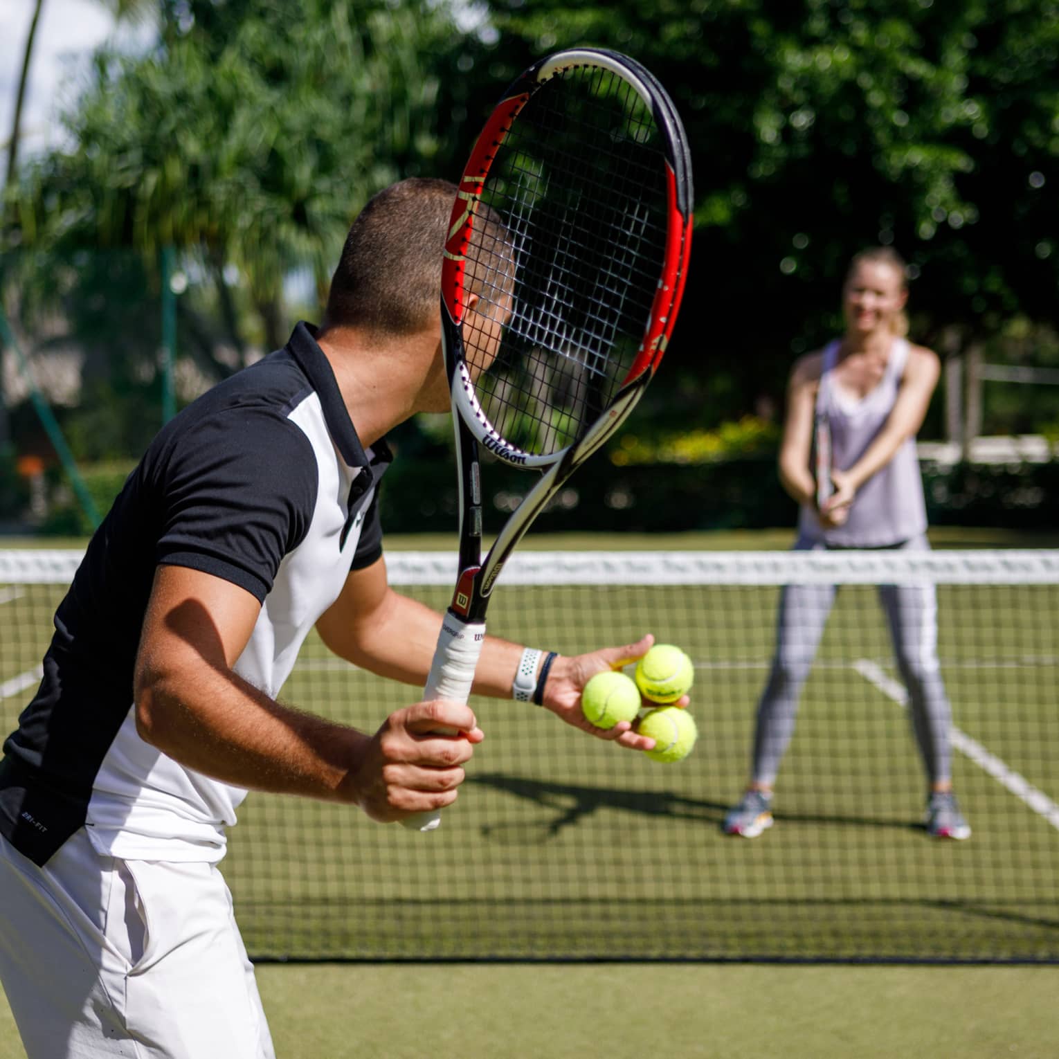 Couple playing tennis on court, man prepares to serve tennis balls to woman ready to swing