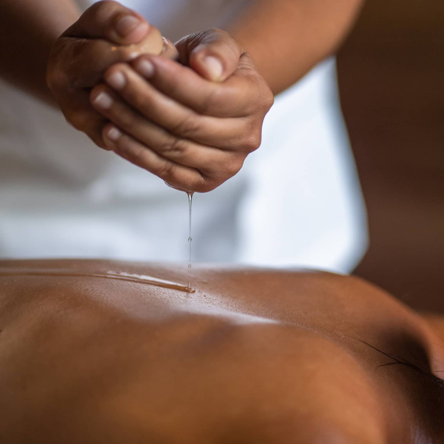 Delicate hands apply oil to a guest's back during a spa treatment