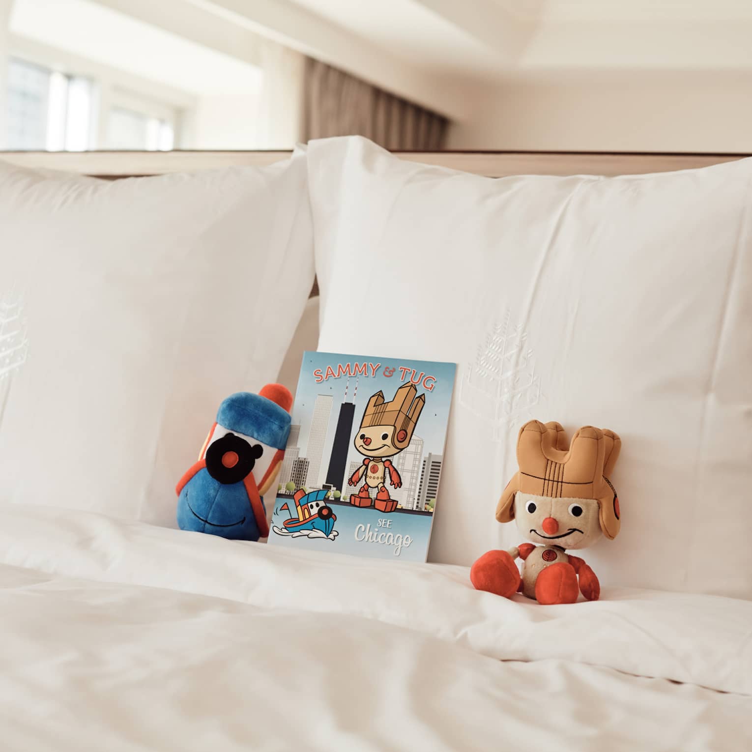 Stuffed animals and a book resting on a white bed.