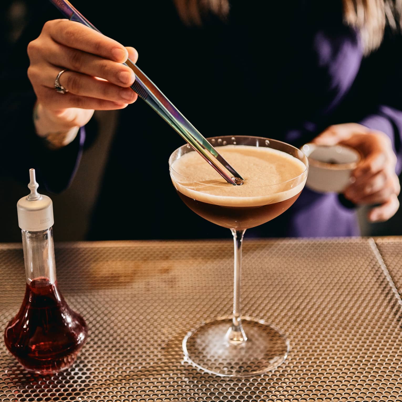 Person standing near a table and stirring a drink in a martini glass