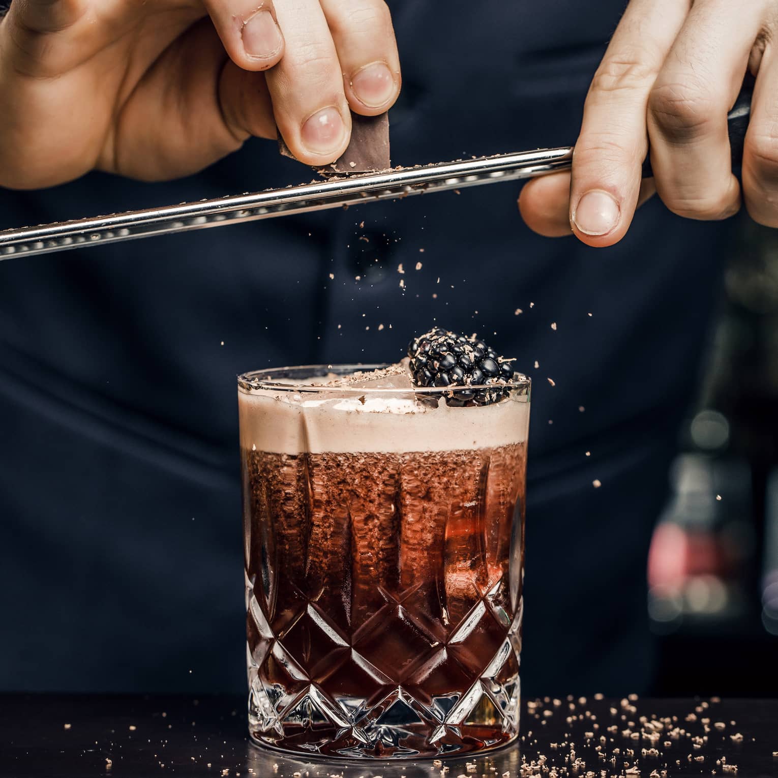 Churchill Club bartender shaves garnish over cocktail in crystal rock glass with blackberry