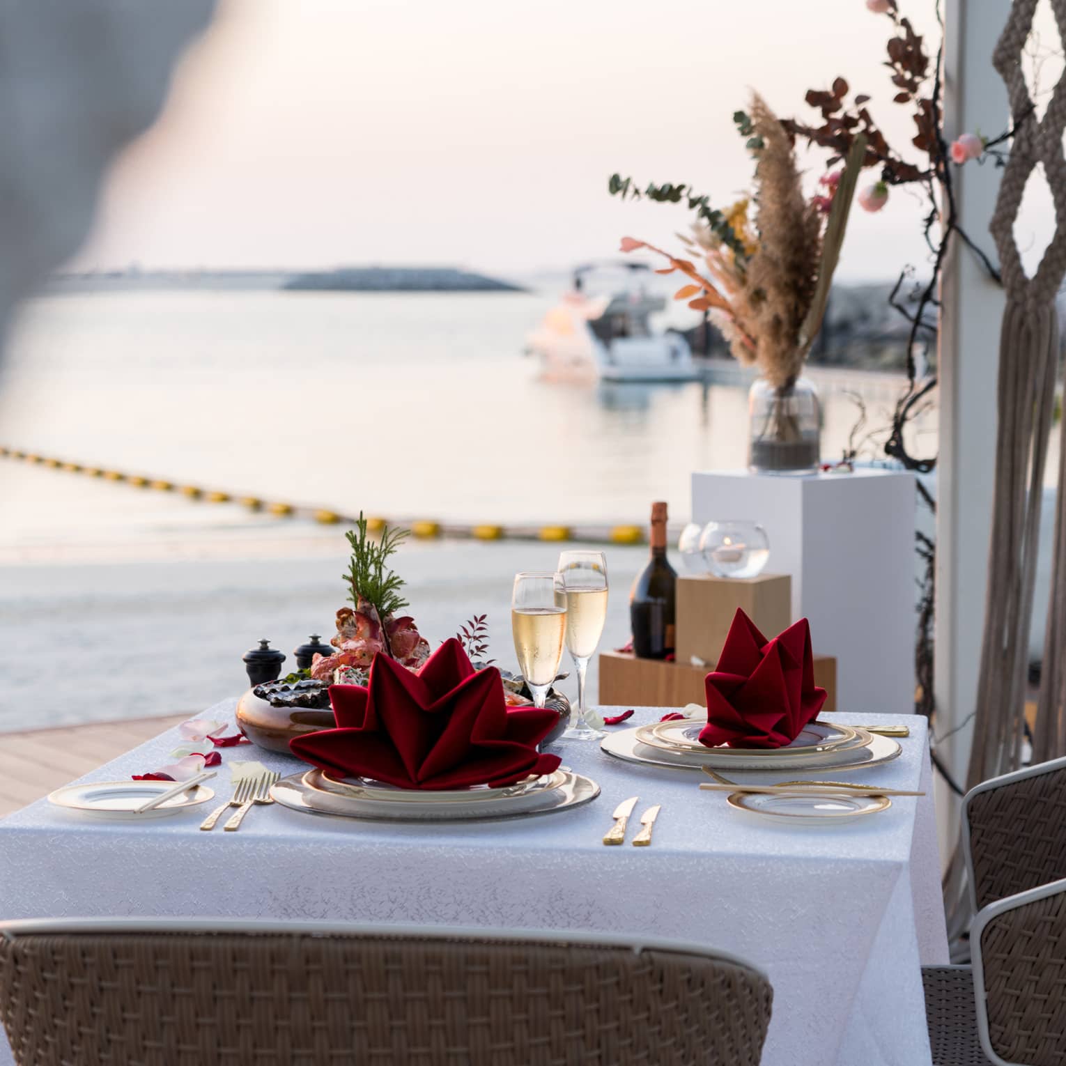 A table set for two with two glasses of champagne on a pier overlooking a calm sea.