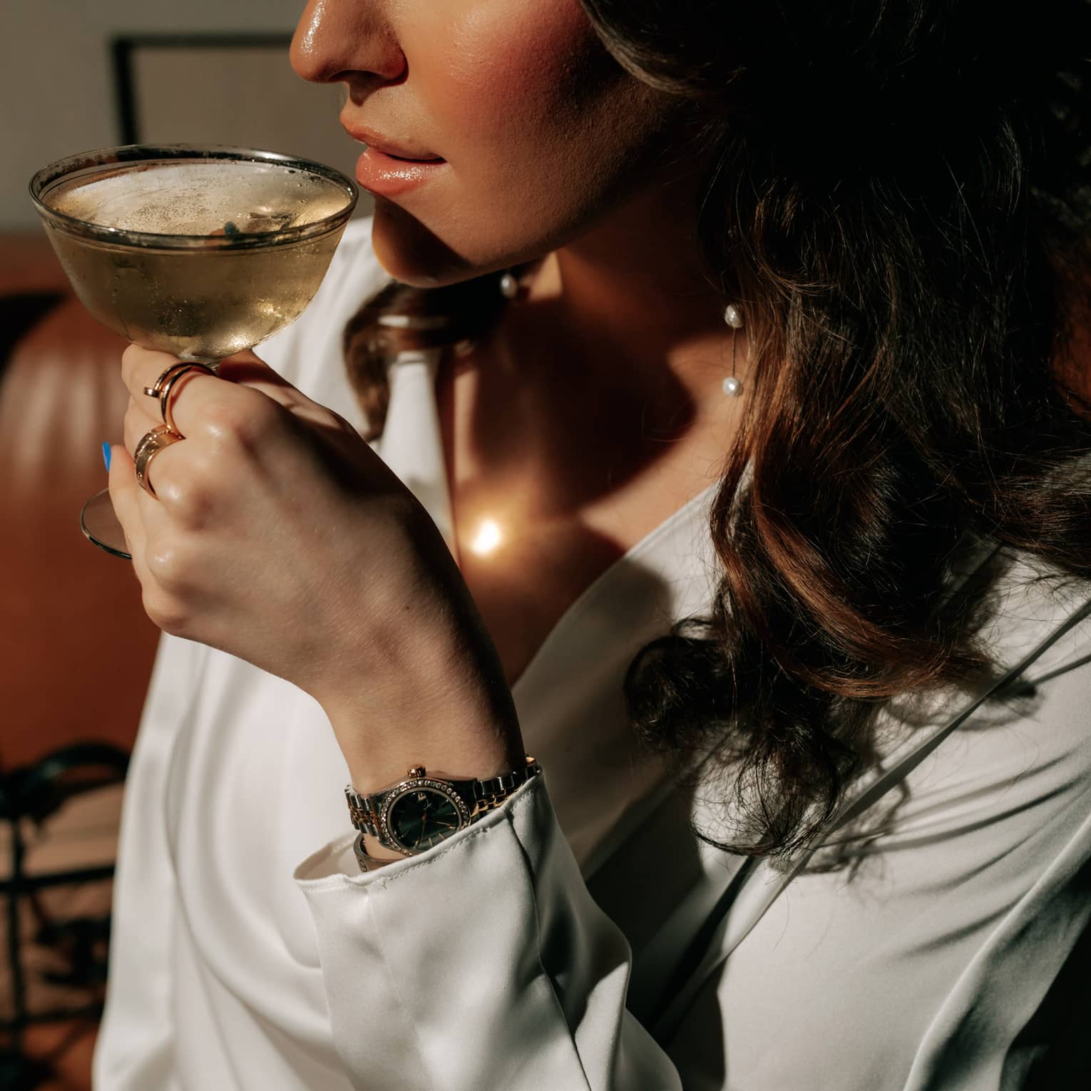 A woman with long, dark hair is about to sip a cocktail from a coupe glass.