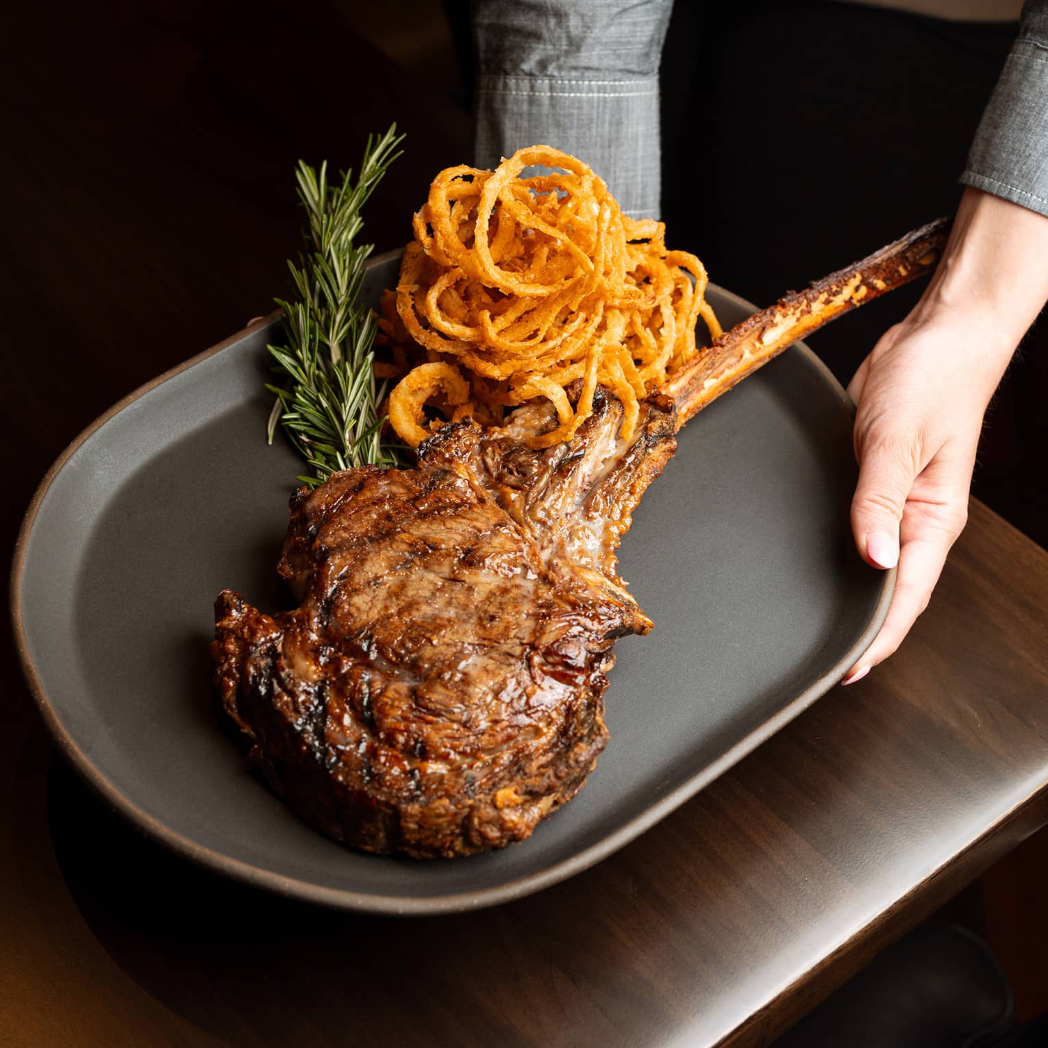 A person serving a large steak and onion rings on a plate