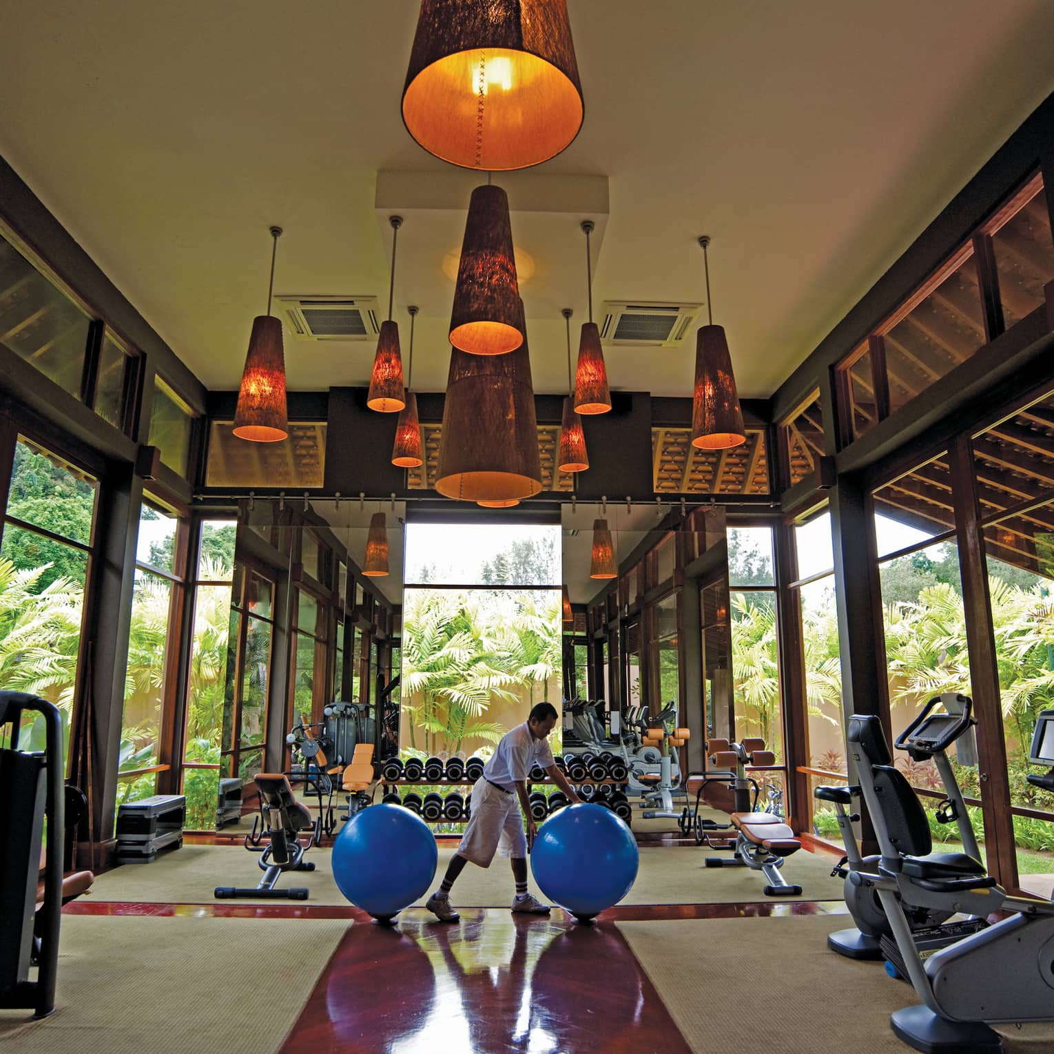 Man rolls blue pilate balls in sunny Fitness Centre with cardio machines