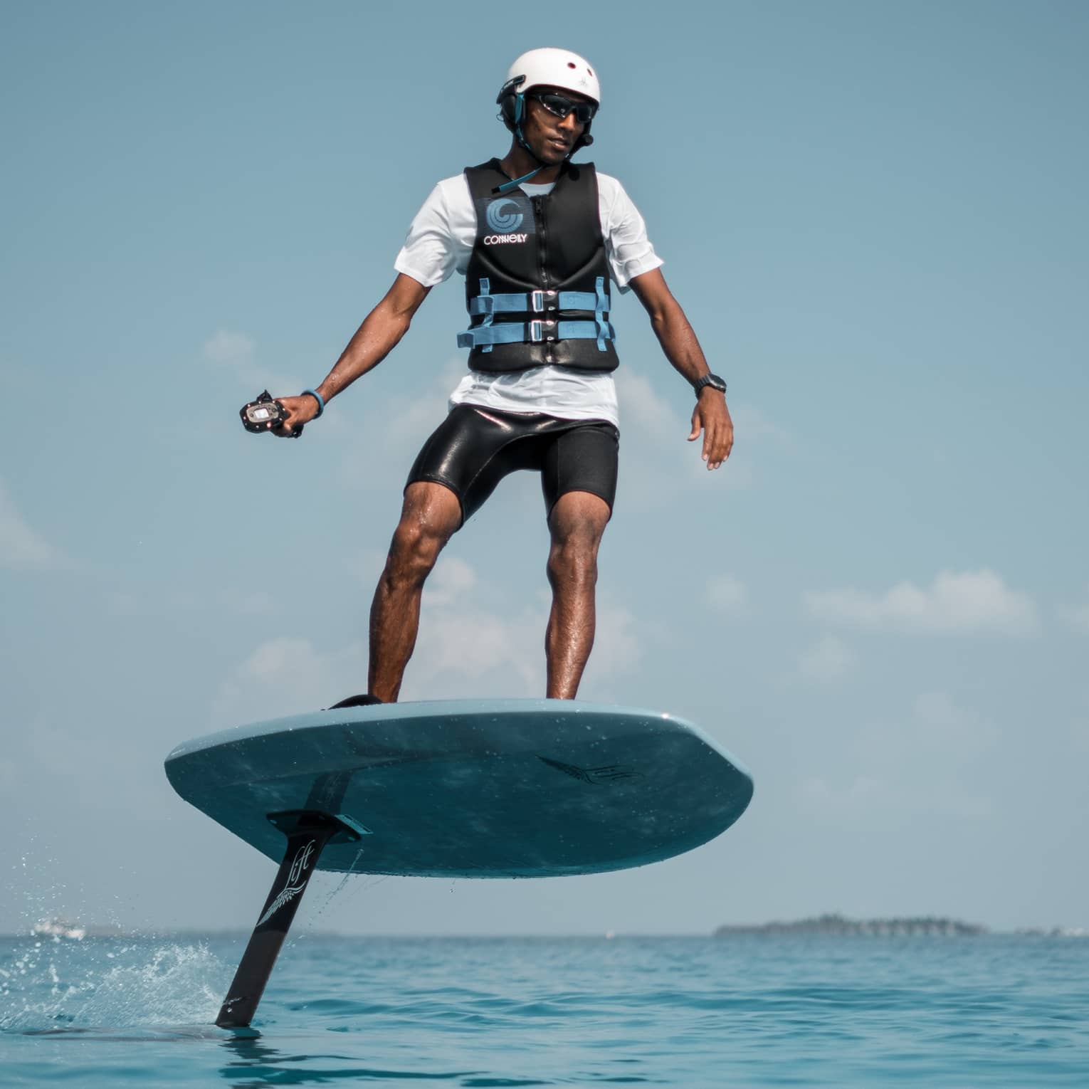 In a helmet and life jacket, an adventurer stands on an eFoil using a handheld control to propel the board out of the water.
