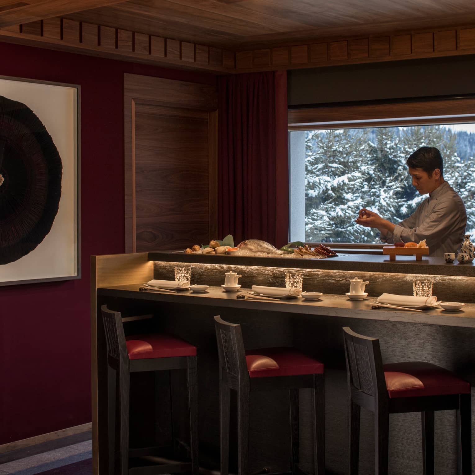 Kaito sushi chef at small bar with fresh whole fish, seafood, window with winter mountain views