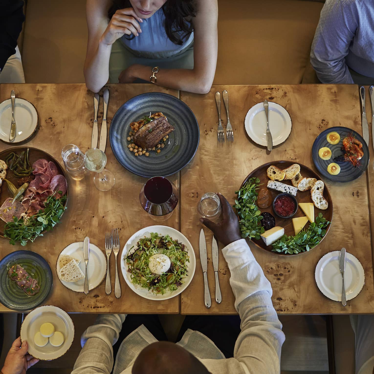 Aerial view of a group dining at a wooden table topped with various vibrant culinary dishes