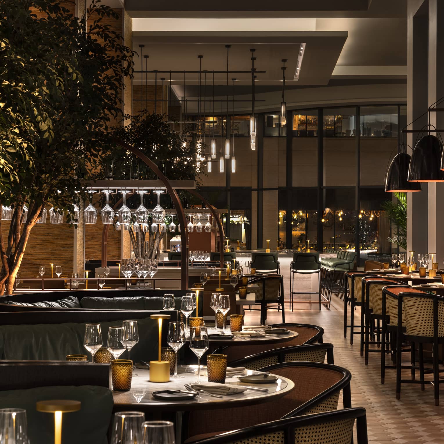 A dimly lit restaurant and bar with large windows, hanging lights, large booths and plants.
