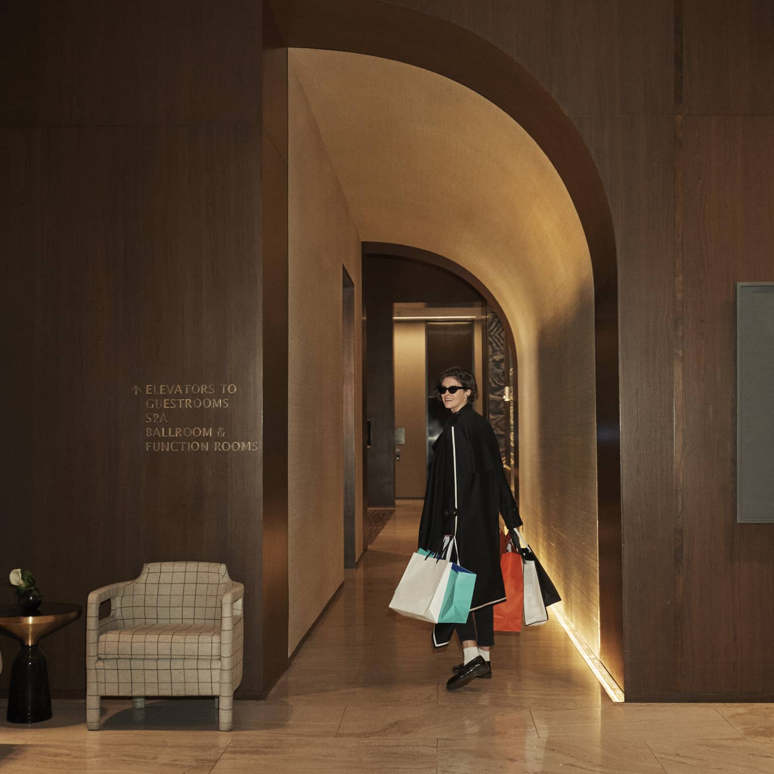 Woman dressed in black clothing and sunglasses, carrying shopping bags.
