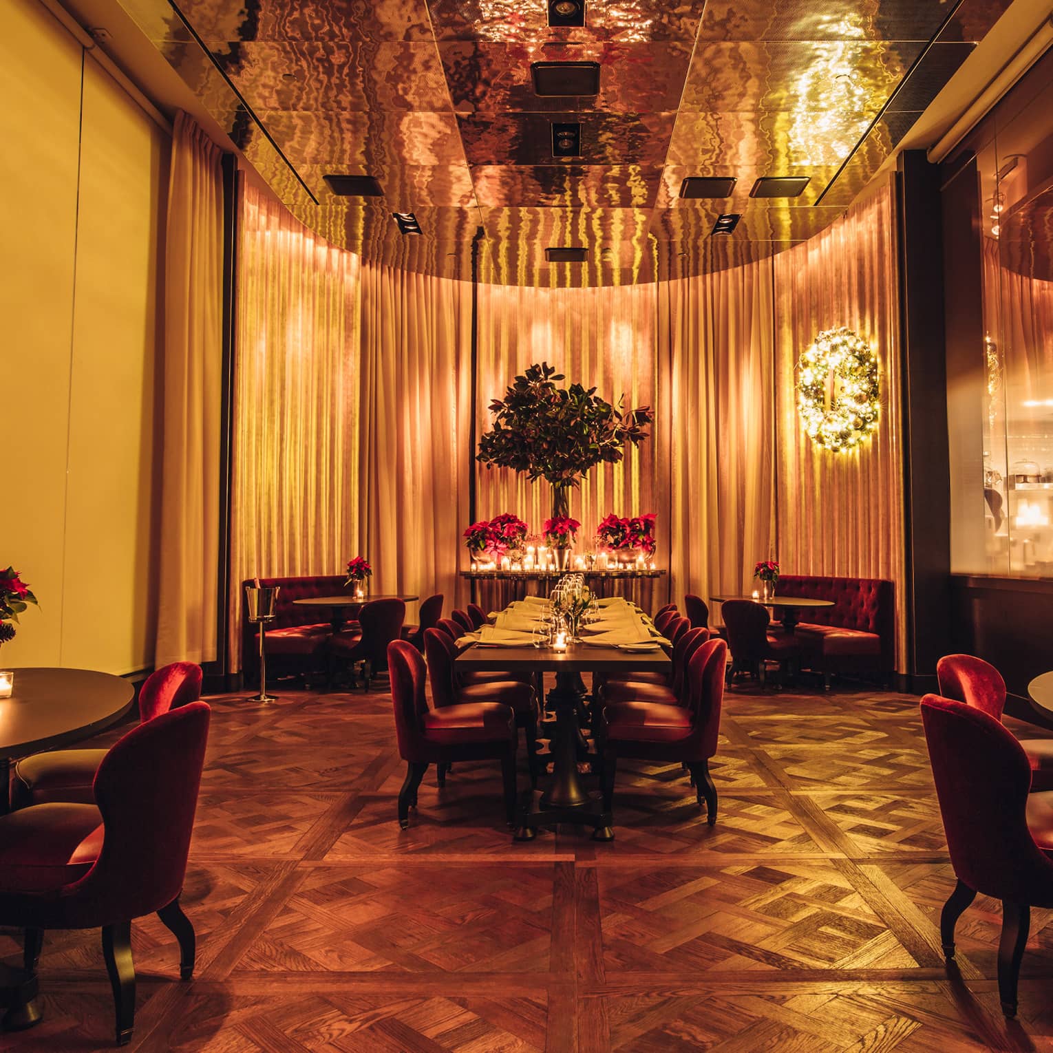 Candle-lit dining area with tables, red velvet lounge chairs, brass accents, tall mirrors and curtains