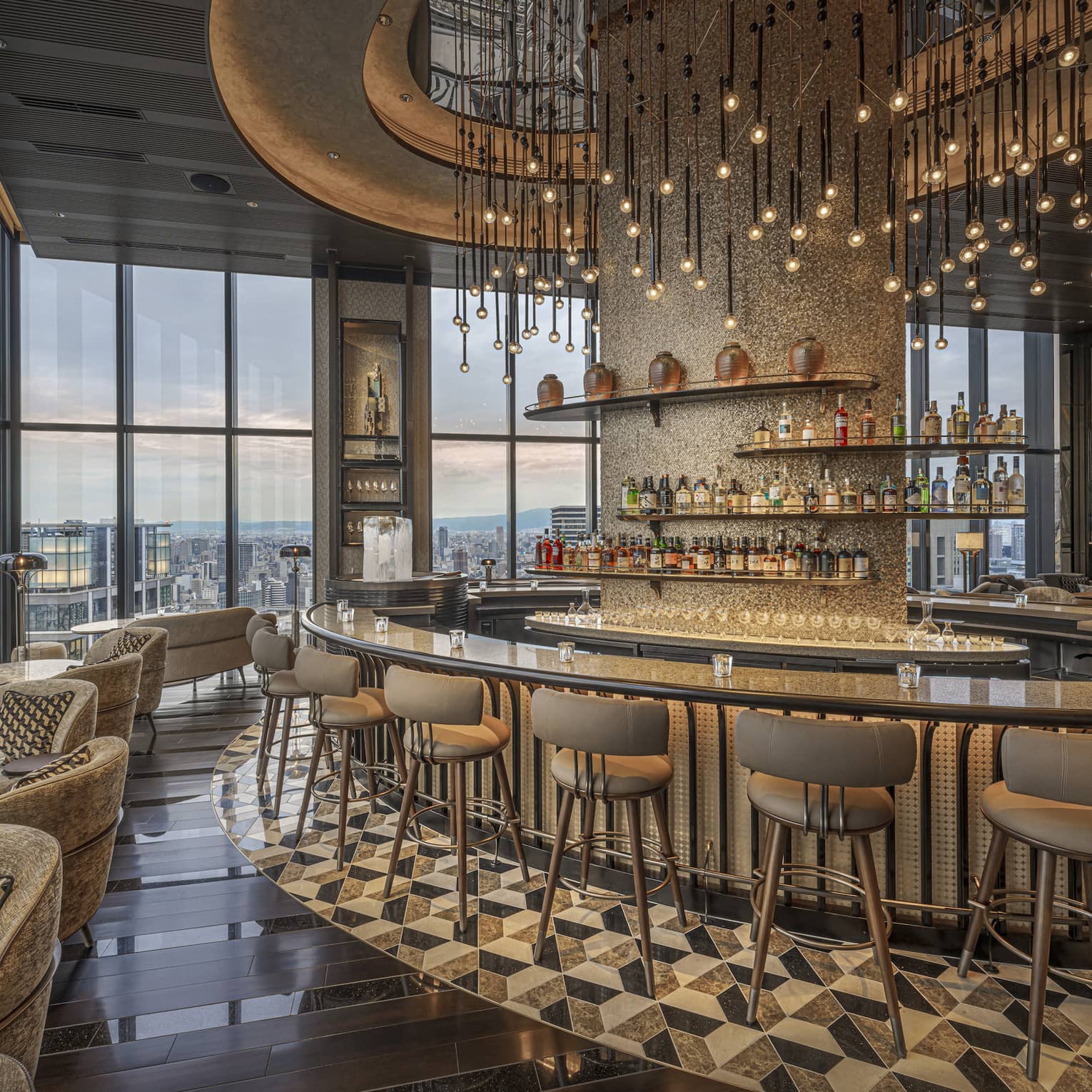Large circular granite-topped bar in a modern luxury restaurant surrounded by a bank of windows overlooking city at dusk.
