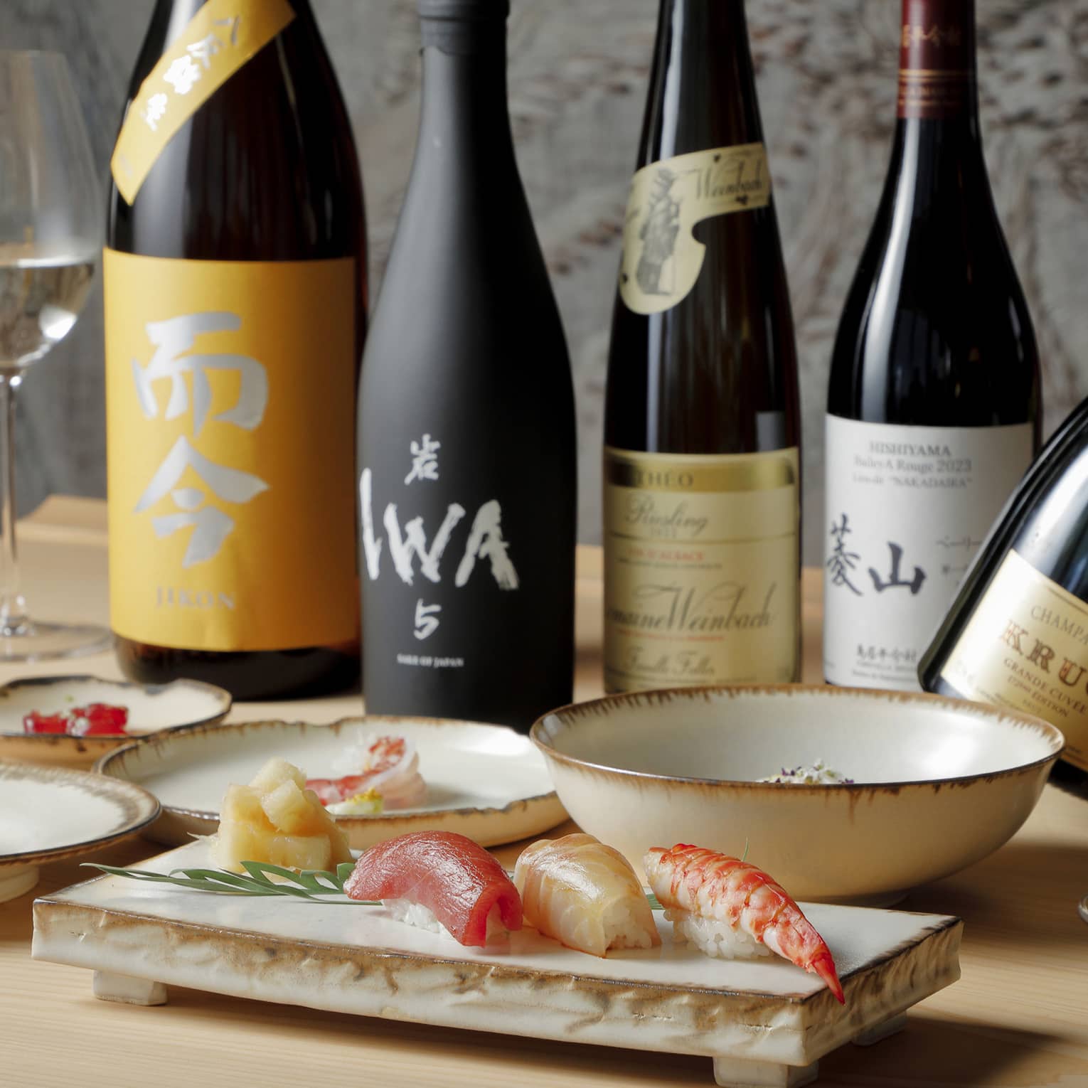 Bottles of sake and Krug champagne and glasses of wine behind dishes artfully laden with vibrant sushi and other delicacies.