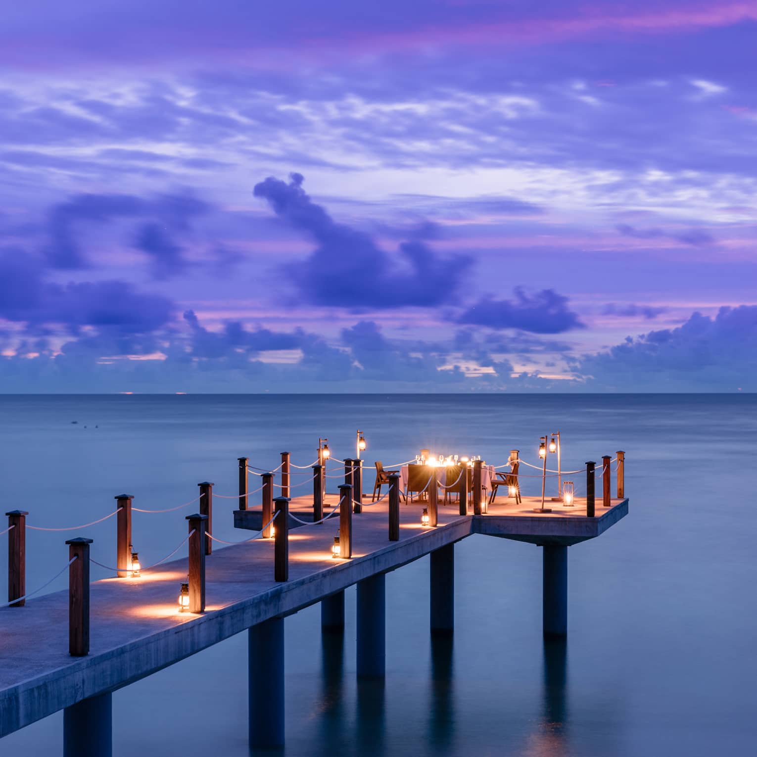Candlelit jetty off Desroches Island with purple sunset hues