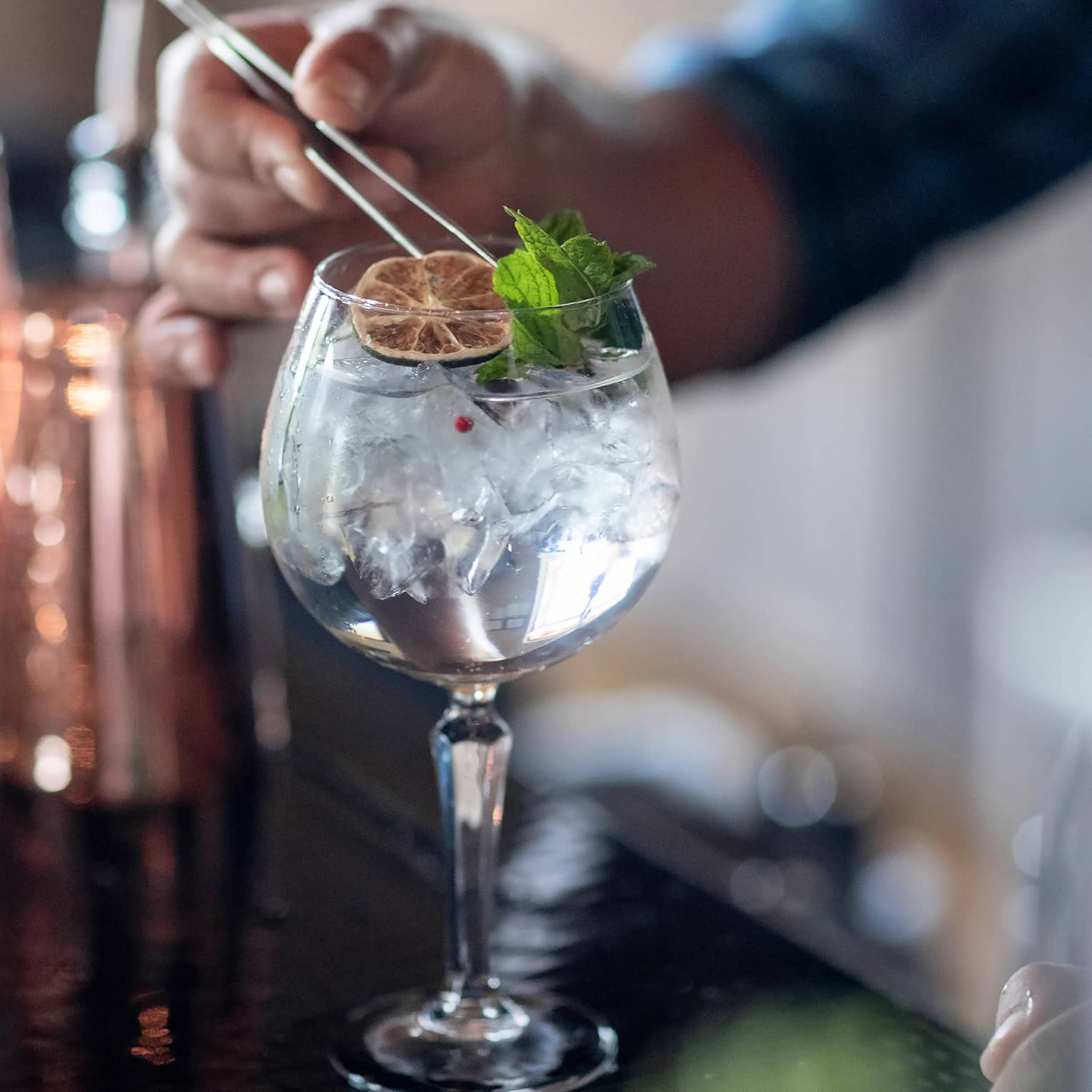 A clear cocktail with an orange wheel and herbs.