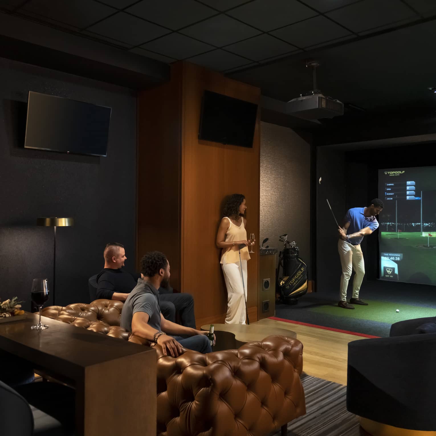A group of people enjoying an indoor golf simulator experience at the luxury hotel Topgolf Swing Suite, with plush seating and a relaxed atmosphere