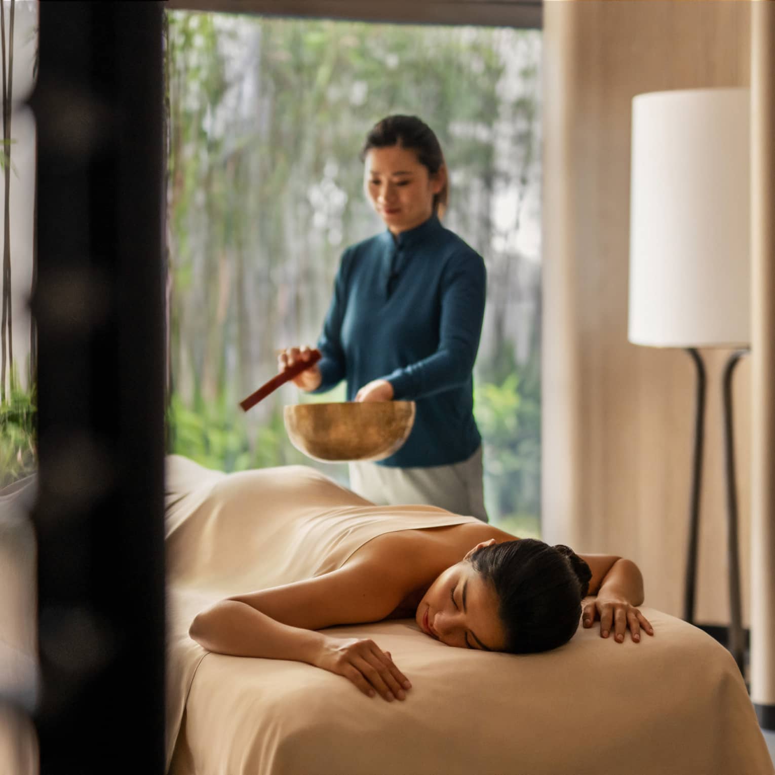Female spa therapist performs singing bowl spa ritual for woman on spa treatment table and luxury hotel spa