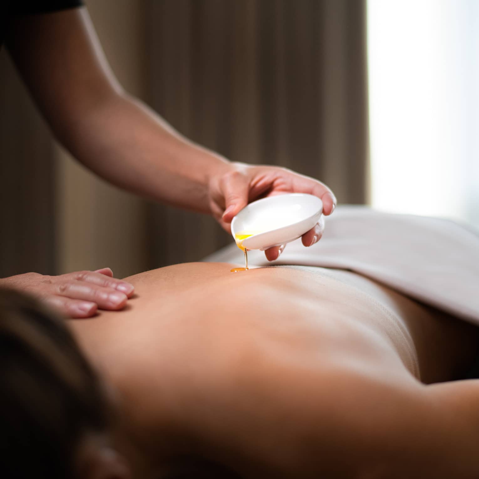 Spa staff pours hot oil on person's back during massage