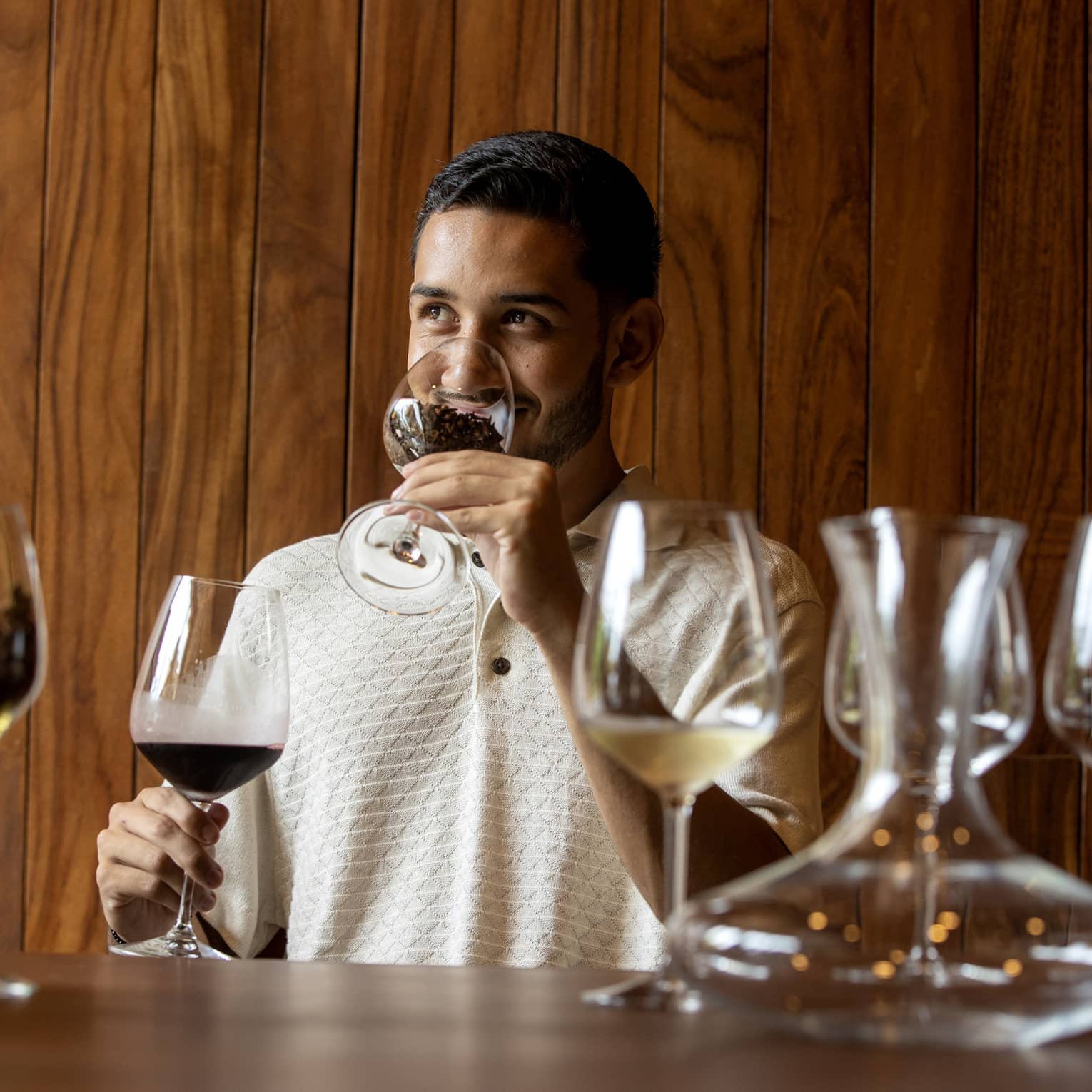 At a wine tasting, a guest smells coffee beans in a glass before tasting the glass of dark red wine held in his other hand.