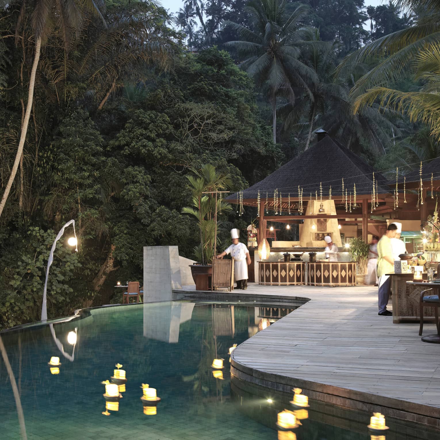 An infinity pool looking out towards the dense jungle; chefs bustle around the outdoor kitchen on the poolside deck.