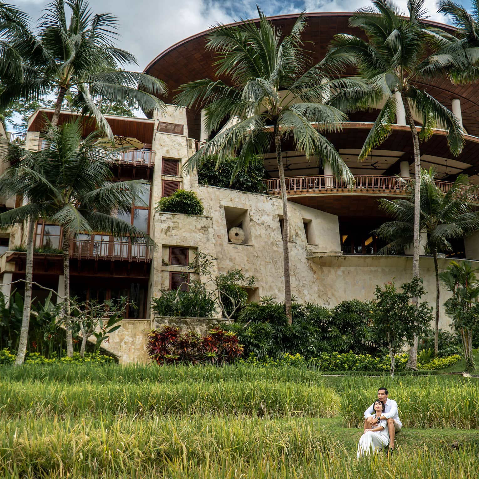 Long view of a couple embracing on the grass in front of the rice-bowl inspired Four Seasons Resort Bali at Sayan.