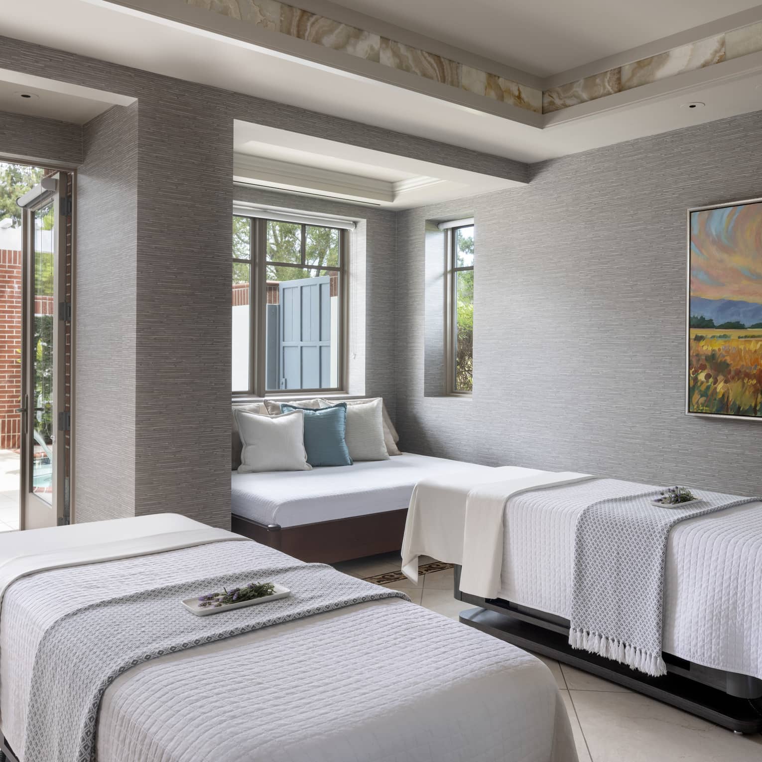 A spa treatment room with two massage beds, a small couch and an open door leading outside.