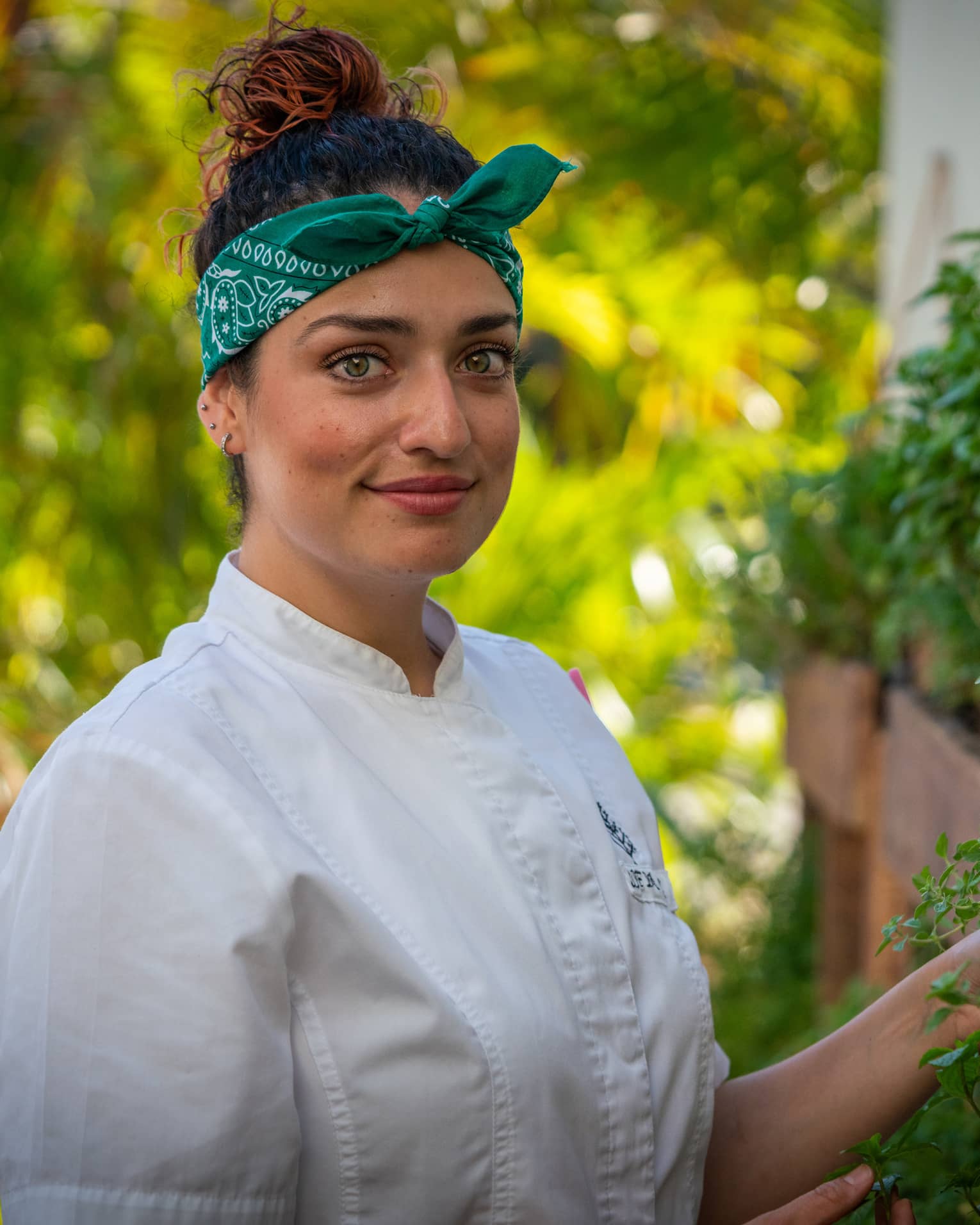 A female chef in a green bandana looking at herbs.