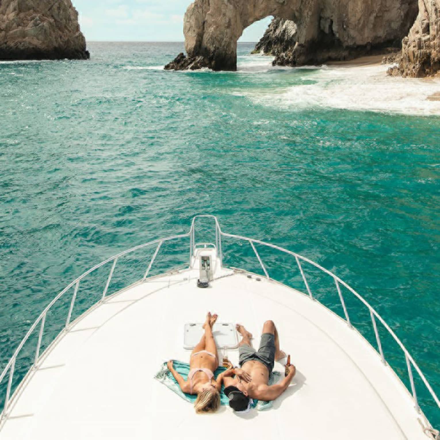 Two people lie on the front of a boat in Cabo